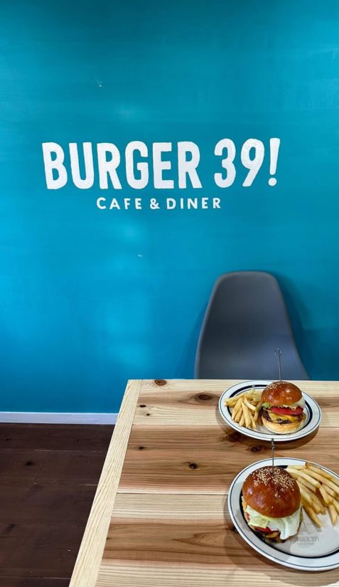 BURGER39！の内観。青色の壁にロゴが描かれている。机と床は木が基調となっている。